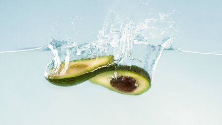 Ripe avocado halves sinking into clear water, blue background