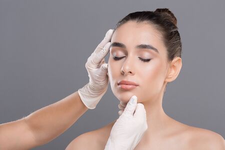 Plastic surgery concept. Young woman on consultation at beautician, grey background