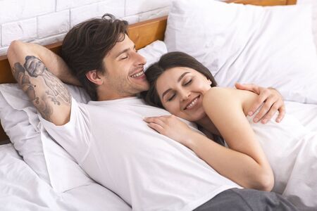 Love and comfort. Happy young couple lying in bed and enjoying closeness, free spaceの写真素材