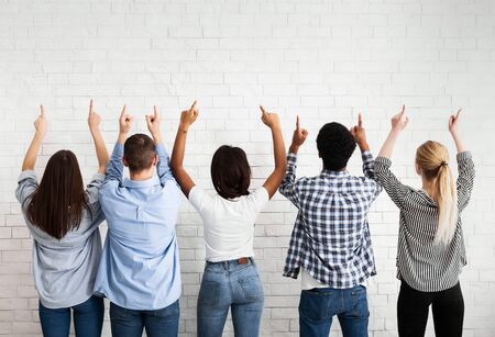 Young people showing free space, pointing fingers up over white brick wallの写真素材