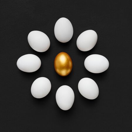 New trends concept. One golden egg surrounded by group of white ones on black background, copy spaceの写真素材