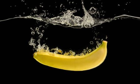 Yellow banana sinking into water with air bubbles, black backgroundの写真素材