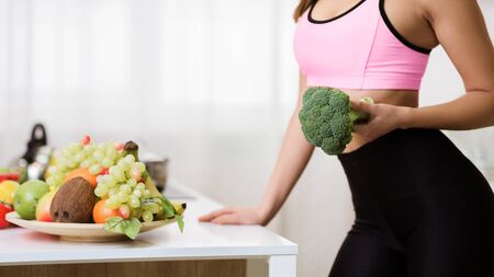 Dieting concept. Girl holding broccoli, cooking healthy salad in kitchen, copy spaceの写真素材