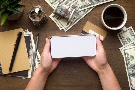 Crowdfunding concept. Modern phone with white blank screen in woman hands on table with money,...