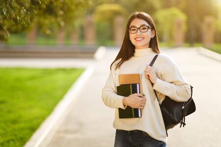 Happy girl posing with backpack carrying books, walking in city parkの写真素材
