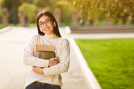 Happy girl with books listening music in campus, smiling to camera, copy spaceの写真素材