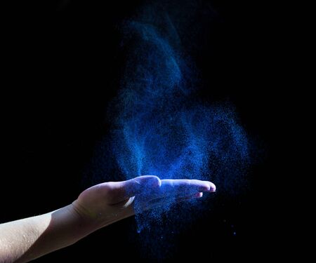Blue holi paint explosion through woman hand on black background, copy spaceの写真素材