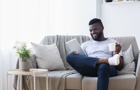 African american man enjoying video on digital tablet and drinking coffee at home, empty spaceの写真素材