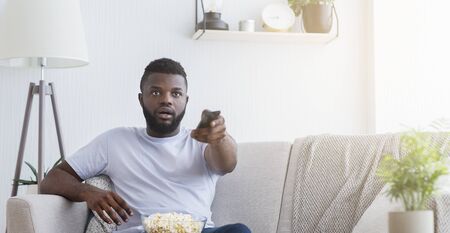 Shocked emotional african american guy watching tv with opened mouth, empty space