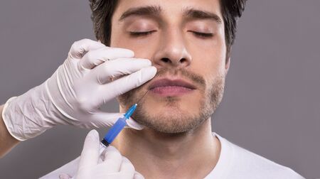 Cosmetology. Young male patient receiving botulinum injection in lips, beauty and skin treatmentの写真素材