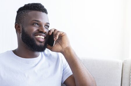 Great worldwide connection. Cheerful young black man talking on smartphone at home, empty space
