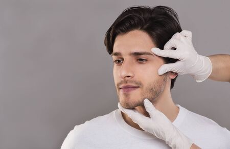 Facial beauty for men. Beautician in gloves touching male patient face, free spaceの写真素材
