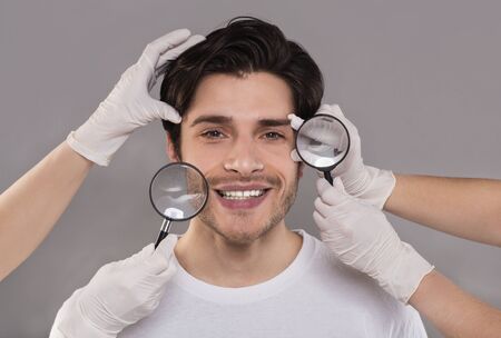 Beauty care and body modification. Beauticians examining young handsome man face through magnifiers