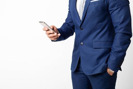 Businessman in blue suit using smartphone on white background. Crop, empty space for textの写真素材