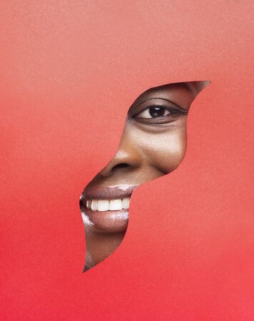 Cheerful african woman smiling through wavy hole in red paper, free spaceの写真素材