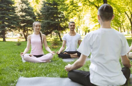 Yoga Teacher And Couple Of Beginners Making Easy Exercises On Fresh Air. Back view Of male instructor, copy spaceの写真素材