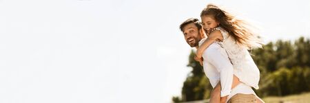 Young father carrying his daughter on back, resting outdoors, panorama, copy spaceの写真素材