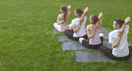 Four young people practicing yoga outdoors, sitting in Vajrasana pose with hands hooked behind the back. Back view, panorama with copy spaceの写真素材