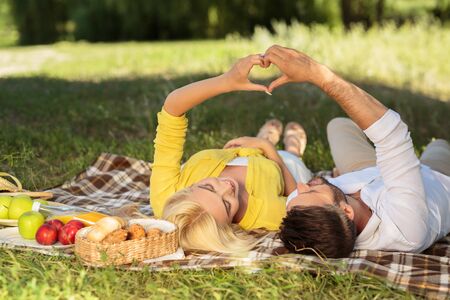 Happy couple in love enjoying day together, lying on plaid in park, making heart symbolの写真素材
