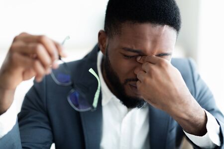 Problems at work. Upset African American businessman massaging his nose bridge holding glasses in hand, closeupの写真素材