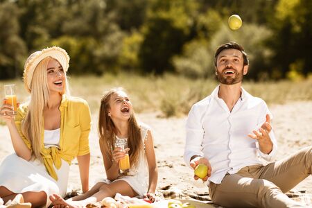 Family picnic. Father juggling with apples, having fun and resting in natureの写真素材