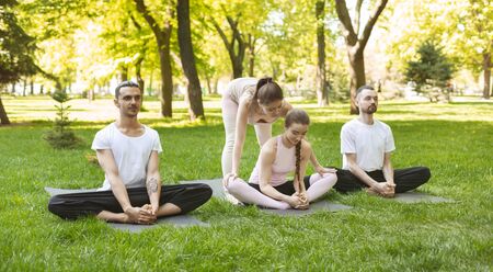 Female Yoga Instructor Helping Young Woman Developing Flexibility During Group Class Outdoors, Panorama With Copy Spaceの写真素材