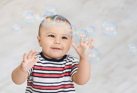 Cute small baby boy playing with many soap bubbles at home, empty space