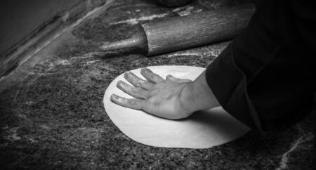 Chef rolling dough for round pizza, closeup, black and white photo