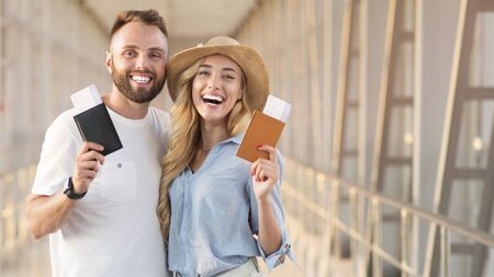 Adorable couple smiling with flight tickets and passports at airport terminal, empty spaceの写真素材