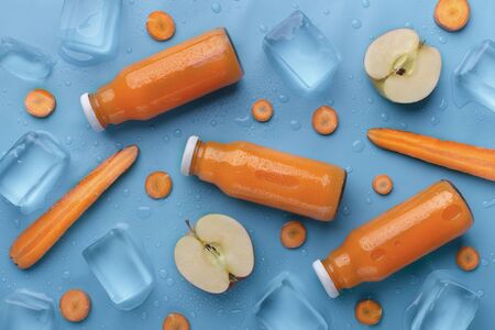 Diet concept. Carrot and apple detox drink in glass bottle for sale on blue background with ice cubesの写真素材