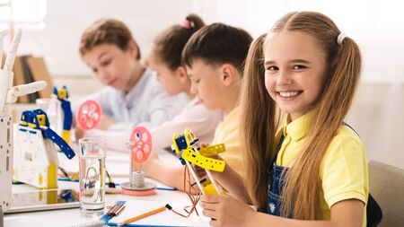 Stem education. Friendly schoolgirl holding robot model in classroom, looking at camera