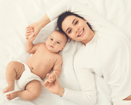 Happy smiling mother and baby lying on bed together, top view