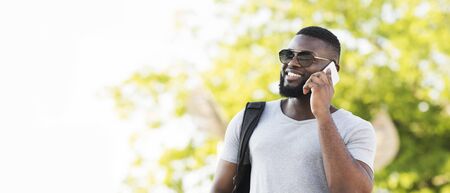 Portrait of stylish african man in sun glasses talking by phone, panorama, copy spaceの写真素材