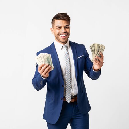 Wealth Creation. Joyful Business Guy Holding Bunch Of Banknotes Over White Studio Background