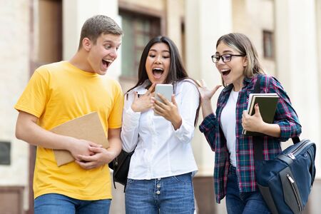 Surprised students checking exam results on smartphone, resting in campus