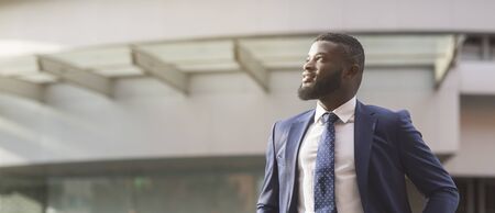 Thoughtful african american businessman looking away standing in front of office building. Panorama with free spaceの写真素材