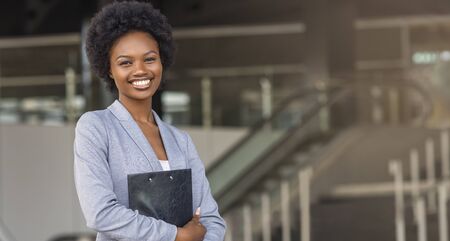 Beautiful Young Afro American Business Woman In Formal Clothes Holding Folder, Looking At Camera And Smiling. Panorama with free spaceの写真素材