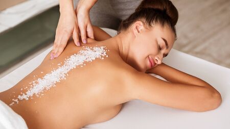 Relaxed woman enjoying salt scrub massage at spa salon, lying with closed eyes