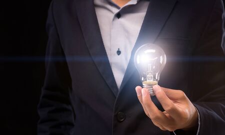 Start up idea. Businessman holding glowing light bulb in hand on black background, panorama