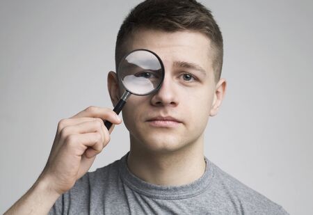 Young man with magnifying glass near eye, close upの写真素材