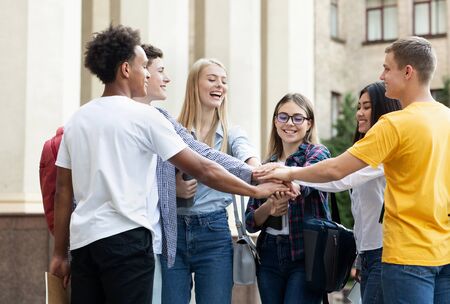 Ready to pass exams. Students stacking hands together in college campusの写真素材