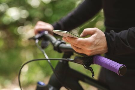 Male Cyclist Holding Sport Bike And Using Cellphone In The Woods, cropped