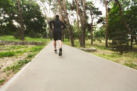 Young Man Jogging In Wooded Park, Training Endurance For Marathon. Rear view with copy spaceの写真素材