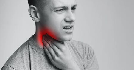 Man suffering with sore throat, touching his neck with hand, monochrome panorama photo with empty...