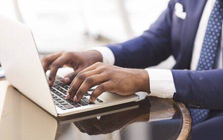 Closeup of afro businessmans hands typing something on laptop in outdoor cafe. Cropped, free spaceの写真素材