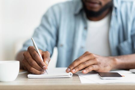 Unrecognizable African American Self-Employee Writing Down His Plans To Notepad. Closeup with copy spaceの写真素材