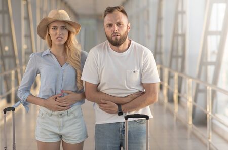 Couple suffering from stomachache, standing at airport terminal, free space