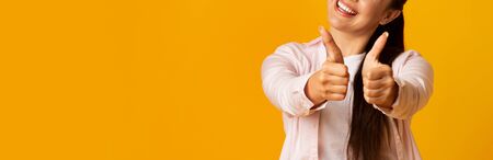 Unrecognizable Girl Gesturing Thumb Up Smiling Widely On Yellow Studio Background. Panorama With...