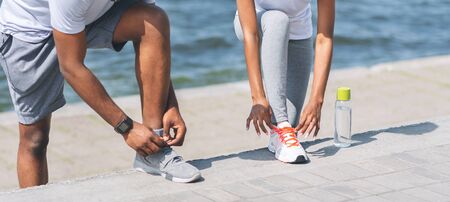 Couple Activities And Jogging. Black Man And Woman Lacing Their Shoes Next To River Embankment. Cropped, Panorama, Copy Spaceの写真素材