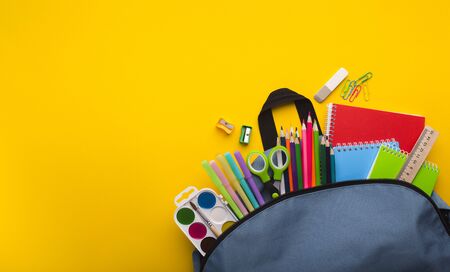 Back to school concept. Backpack with stationery inside on yellow background with free space,...